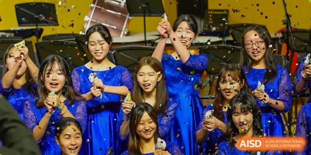 A group of students in blue gowns celebrating joyfully with confetti during a school performance at Tianjin International School (TIS).