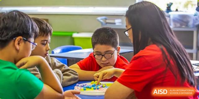 A young boy with glasses focusing intently on a colorful tabletop game or educational activity in a classroom at Tianjin International School (TIS).
