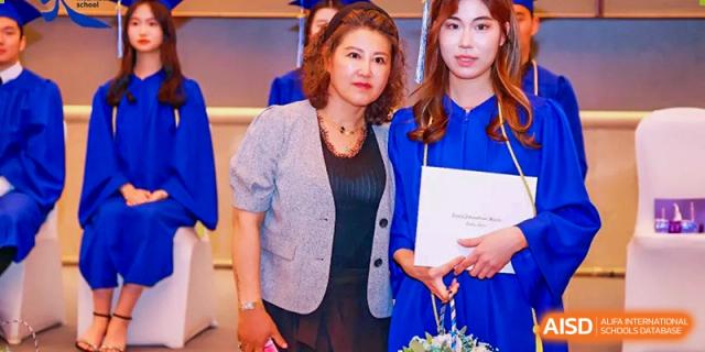 A graduate in a blue gown posing for a photo with a family member while holding her diploma at Tianjin International School (TIS).
