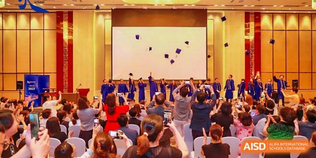 Graduates on stage throwing their caps into the air as the audience cheers during a graduation ceremony at Tianjin International School (TIS).