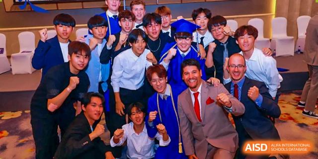 A large group of male students and a teacher in a suit cheering and posing together during a graduation celebration at Tianjin International School (TIS).