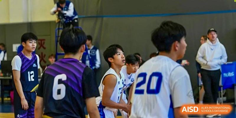 A young male basketball player in a white jersey looks upward during a game on an indoor court at Tianjin International School (TIS).