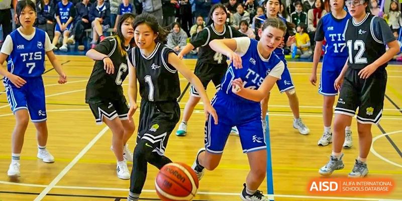 Two basketball players, one in black and one in blue, compete for the ball during a fast-paced game at Tianjin International School (TIS).