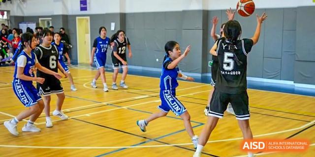 A female basketball player in a blue uniform sprints down the court during a competitive indoor match at Tianjin International School (TIS).