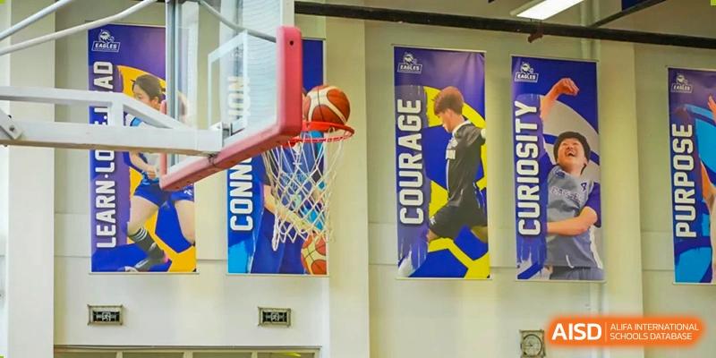 A basketball enters the hoop during a game, with motivational banners hanging on the gymnasium wall at Tianjin International School (TIS).