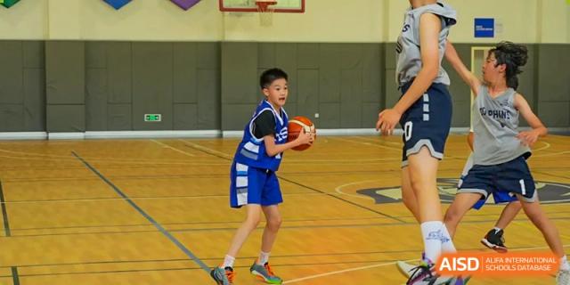 A young boy in a blue and white basketball jersey focuses on the court while holding a basketball during a game at Tianjin International School (TIS).