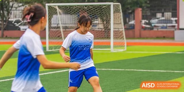 A girl wearing a blue and white sports kit runs across a green soccer field during an outdoor athletic event at Tianjin International School (TIS).