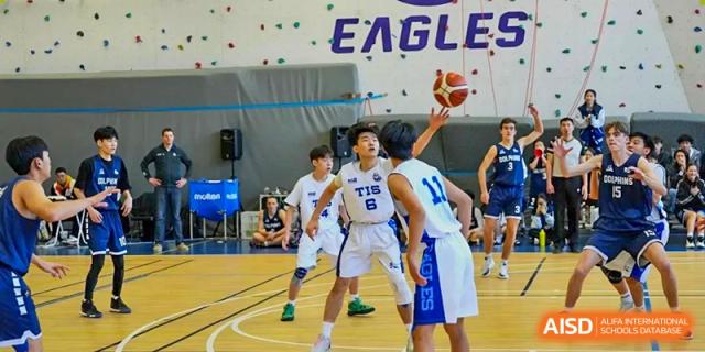 A male basketball player in a white "Eagles" jersey defends the court during a match at Tianjin International School (TIS).