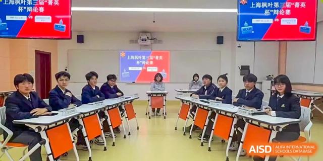 Students sit around a table in a classroom, viewing a presentation displayed on a front projector screen during an engaging academic discussion or seminar at Maple Leaf International School Shanghai.