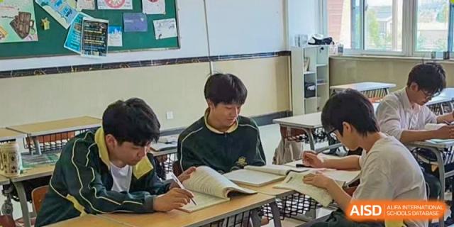 Two male students sit together at a classroom desk, deeply focused on reading and studying from large, open textbooks during a quiet session at Maple Leaf International School Shanghai.