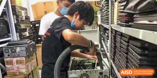 A student wearing a protective mask works diligently on the internal hardware components of a computer or server within a technical lab setting at Maple Leaf International School Shanghai.