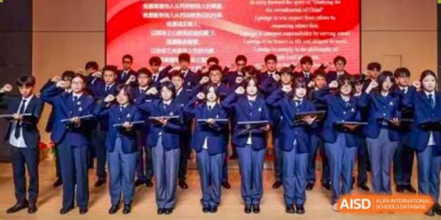 A large group of students stands in formation, all holding red documents and giving a uniform salute with their hands over their hearts at Maple Leaf International School Shanghai.