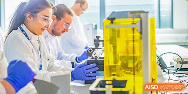 A male researcher wearing blue gloves works intensely with scientific apparatus, including a bright yellow piece of equipment, inside a focused laboratory setting at Maple Leaf International School Shanghai.