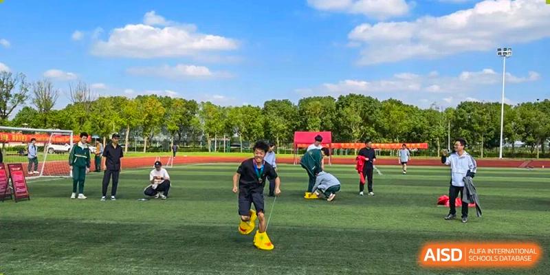 Students on the sports field participate in an active relay race, running in oversized yellow shoes under a blue sky, demonstrating teamwork at Maple Leaf International School Shanghai.