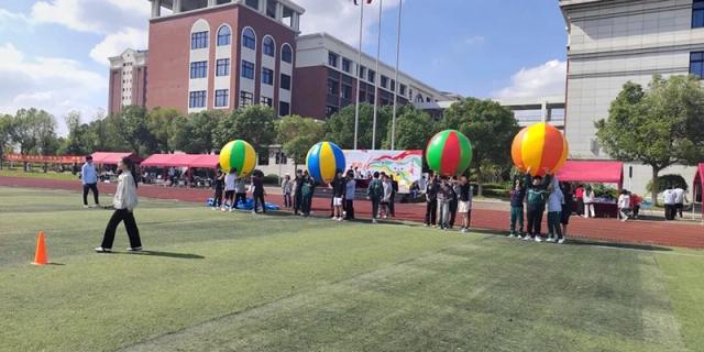 An organized school event takes place on a grassy area outside the main buildings, featuring large, colorful inflatable balls and a crowd of student attendees at Maple Leaf International School Shanghai.