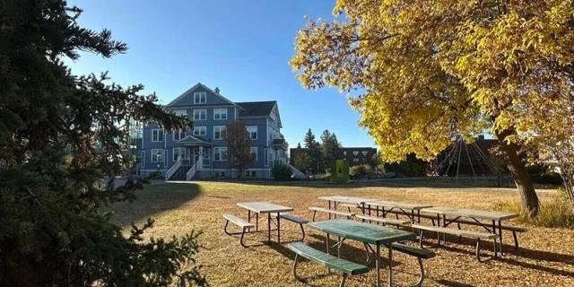 A traditional-style campus house overlooks an autumnal lawn with picnic tables and large, yellow-leafed trees, providing a classic, serene outdoor setting at Maple Leaf International School Shanghai.