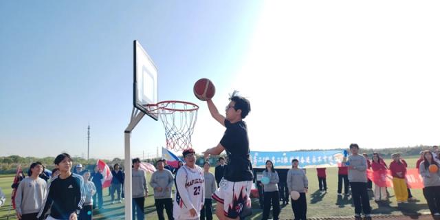 An energetic male student leaps high to perform a dunk during an enthusiastic basketball game while spectators gather to watch the exciting action unfold at Maple Leaf International School Shanghai.