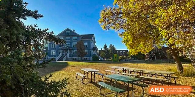 A traditional-style campus house overlooks an autumnal lawn with picnic tables and large, yellow-leafed trees, providing a classic setting at Maple Leaf International School Shanghai.