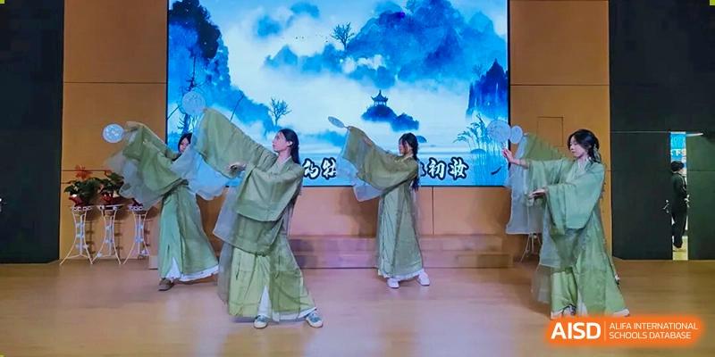 Two students perform a graceful cultural dance in light green robes on a stage, with a scenic backdrop featuring a traditional Chinese painting at Maple Leaf International School Shanghai.