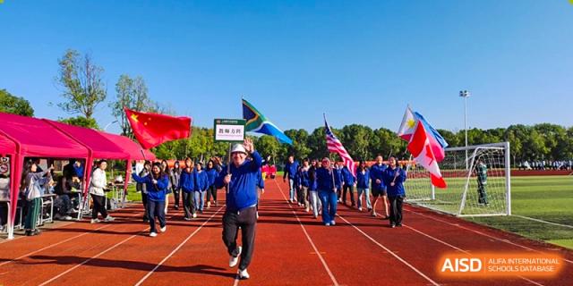 Students dressed in blue and led by a person carrying a banner march in a procession on a running track during an opening ceremony at Maple Leaf International School Shanghai.