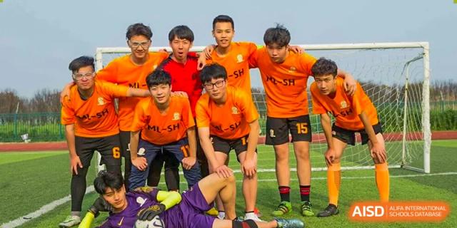A cheerful school soccer team wearing bright orange jerseys poses together on the field after a game or practice session at Maple Leaf International School Shanghai.