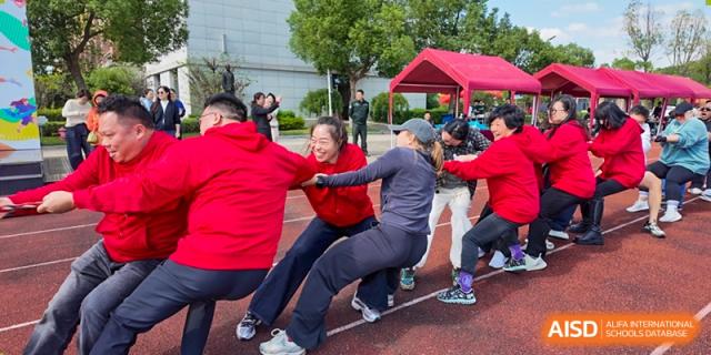 A group of people, including students in red jackets, engages in a competitive tug-of-war game during an outdoor sports event at Maple Leaf International School Shanghai.