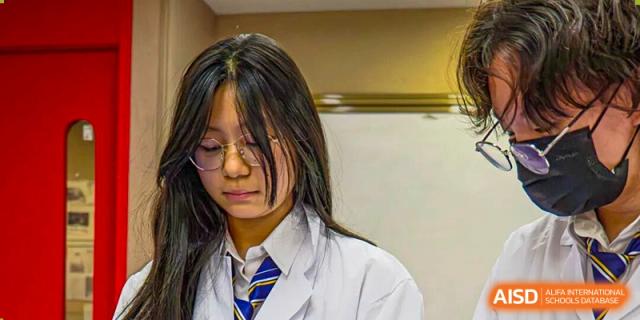 A dedicated female student wearing a lab coat and glasses looks down, possibly conducting research or studying in a laboratory environment at Living Word Shanghai.