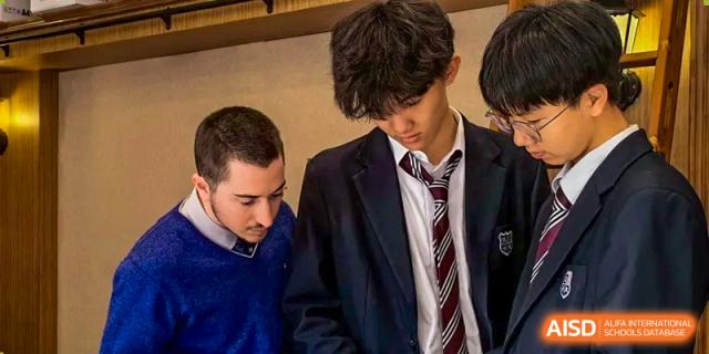 Two high school male students in blazers and ties, one offering instruction, during a serious discussion at Living Word Shanghai.