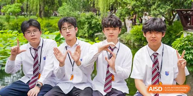 Two male students in white school shirts and ties hold up whistles, making heart shapes with their hands in a bright outdoor environment. Living Word Shanghai
