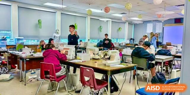A group of students and adults collaborating around a large table in a classroom setting, working on a project with various materials. Living Word Shanghai