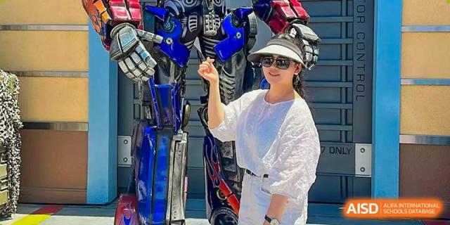A female student wearing sunglasses and a sparkly white top stands outdoors, holding up a collection of what appear to be colorful athletic straps or bands. Living Word Shanghai