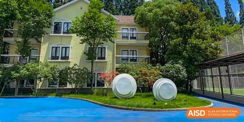 A peaceful image of the school's dormitory or teaching building exterior, featuring a green lawn and modern, abstract white sculptures, Living Word Shanghai.