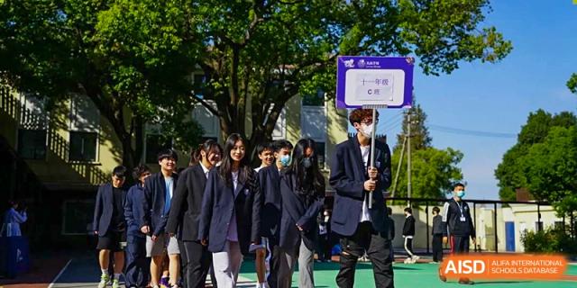 A group of students in dark blazers and uniforms posing together for a photo next to a school banner outdoors, Living Word Shanghai.