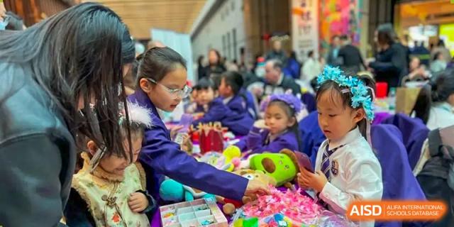 Young students in purple school attire participating in a colorful, hands-on activity or market event in a crowded outdoor area, Living Word Shanghai.
