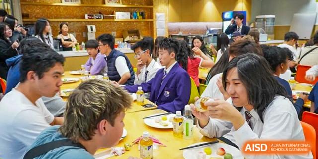 Students in a cafeteria or restaurant are seated at a table, enjoying a meal together, some in school uniforms or formal attire. Living Word Shanghai
