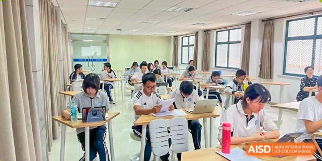 Students in matching white shirts diligently taking notes and working at individual desks in a brightly lit, focused classroom environment at Jian Ping High School.
