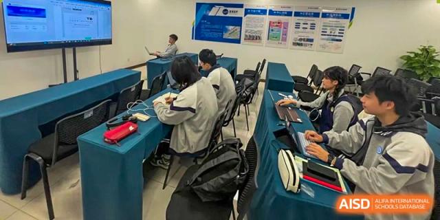 A group of students collaborating and working on laptops around a small table, likely for a group project, in a modern classroom setting at Jian Ping High School.