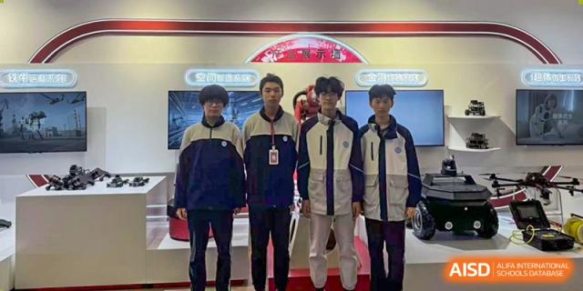 Four male students in school uniforms posing together in front of an exhibition backdrop, representing an academic event at Jian Ping High School.
