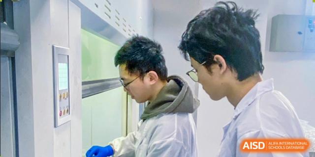Two male students in lab coats work together in a fume hood, conducting a science experiment in the laboratory at Jian Ping High School.