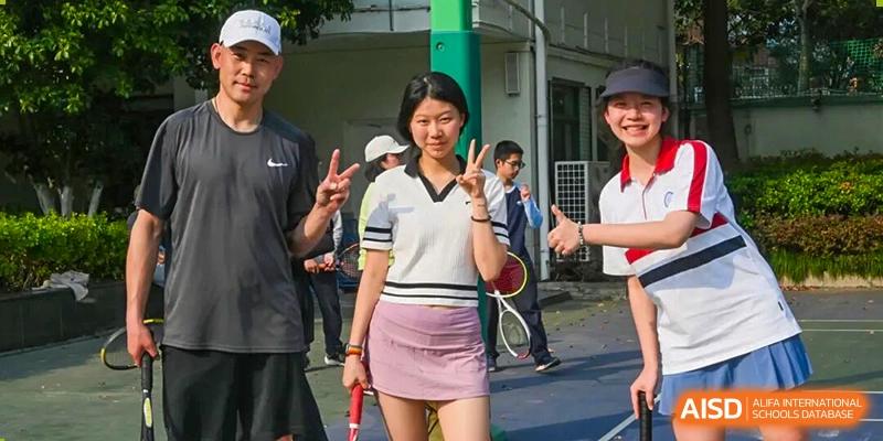 A smiling female student holds a tennis racket and gives a peace sign, flanked by two male students, Jian Ping High School.