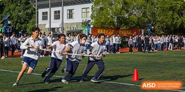 A group of male students in uniforms aggressively pulls a rope during a vigorous outdoor tug-of-war competition on a green field, Jian Ping High School.