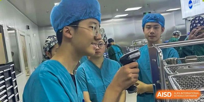 A young man wearing scrubs and glasses, holding a medical scanner or device, appearing to be in a hospital or lab setting, Jian Ping High School.