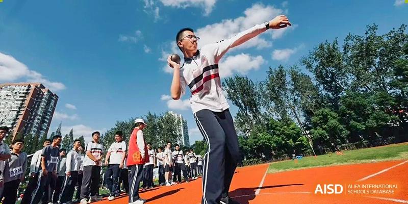 A male student in athletic wear throwing a shot put on a track field during a competition, with other students watching, Jian Ping High School.