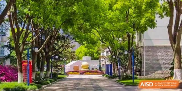 A wide, paved path on a university or school campus lined with tall, lush green trees and manicured lawns, Jian Ping High School.