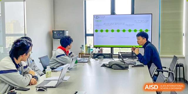 A student with red and blue hair sitting at a long table in a modern conference room with a large screen displaying a timeline chart, Jian Ping High School.
