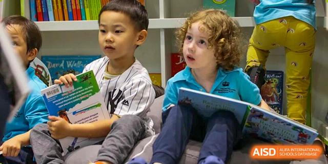 A young boy and girl are sitting side-by-side, holding books and looking up with interest, attentive to their teacher or a story at The British International School Shanghai, Puxi.