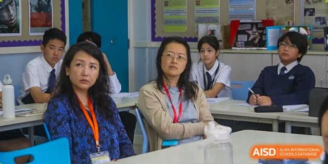 A mix of adults and students are seated and listening intently, indicating their concentration during a school presentation or assembly at The British International School Shanghai, Puxi.