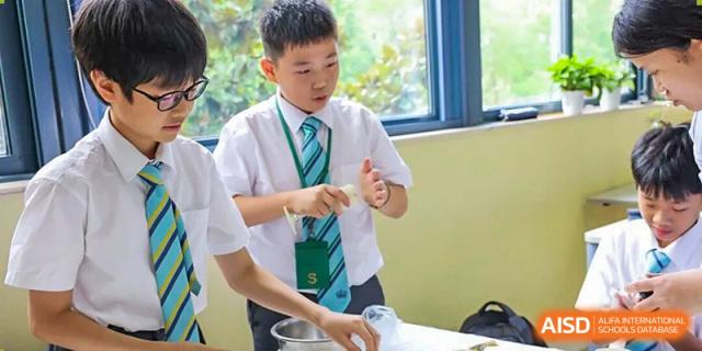 A young male student in school uniform is participating in a hands-on activity, possibly a science experiment, at The British International School Shanghai, Puxi.