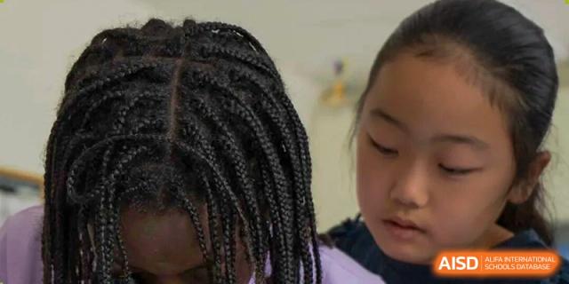 Close-up of two young female students, one with braided hair and one of East Asian descent, focused on a collaborative learning activity at The British International School Shanghai, Puxi.