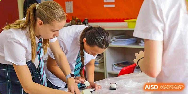 A teacher wearing a striped tie actively assisting several students with a hands-on learning activity at a table in the classroom at The British International School Shanghai, Puxi.